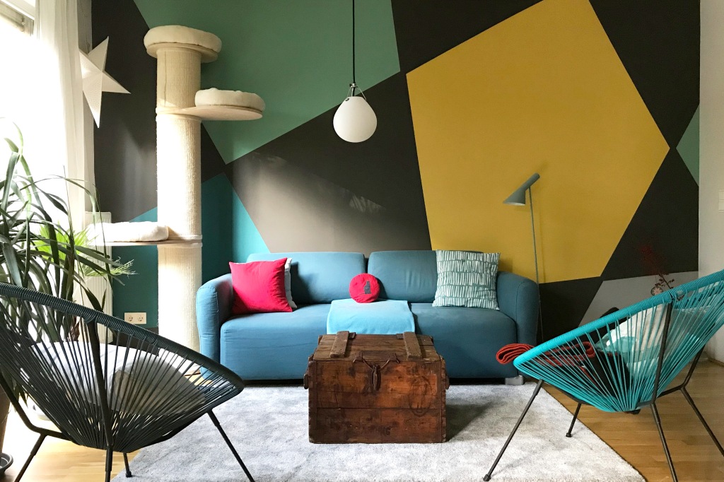 Wohnzimmer mit einer mit minimalistischen Formen gestalteten wand hinter Sofa, Lampen und Sesseln.