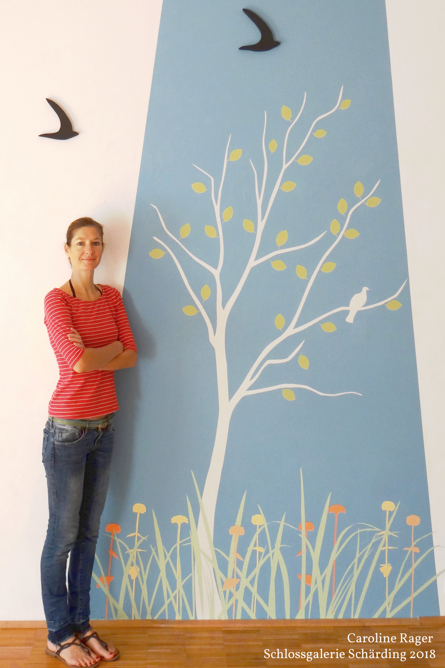 Wandmalerei mit Baum, Wiese und Blumen. Über den Blumen fliegen schwarze Vögel. 